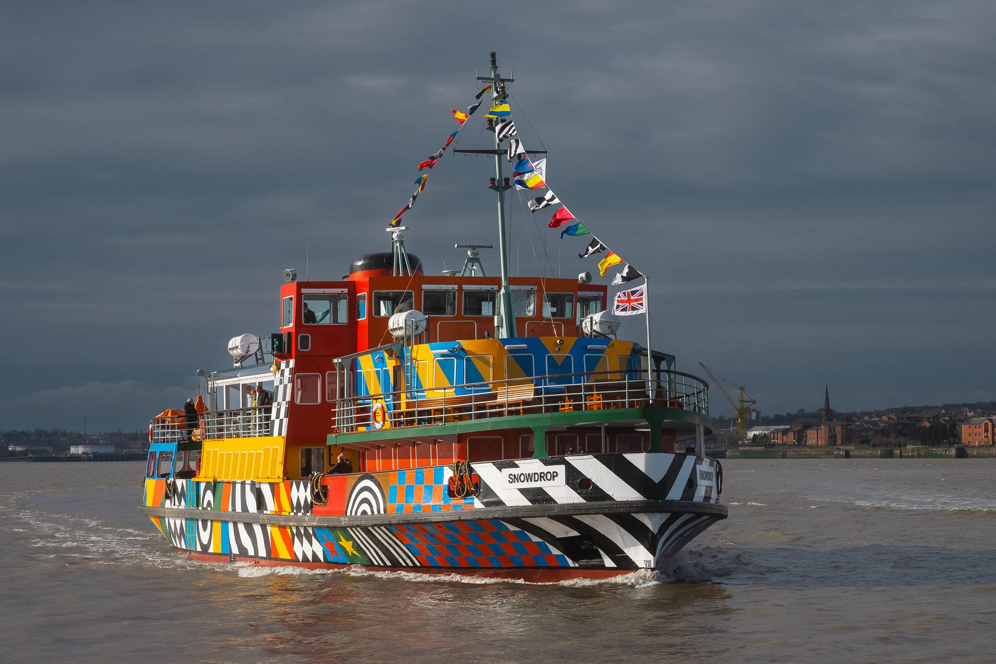 The Snowdrop ferry on the River Mersey, decorated in a striking design by Sir Peter Blake, sails past the Liverpool waterfront.