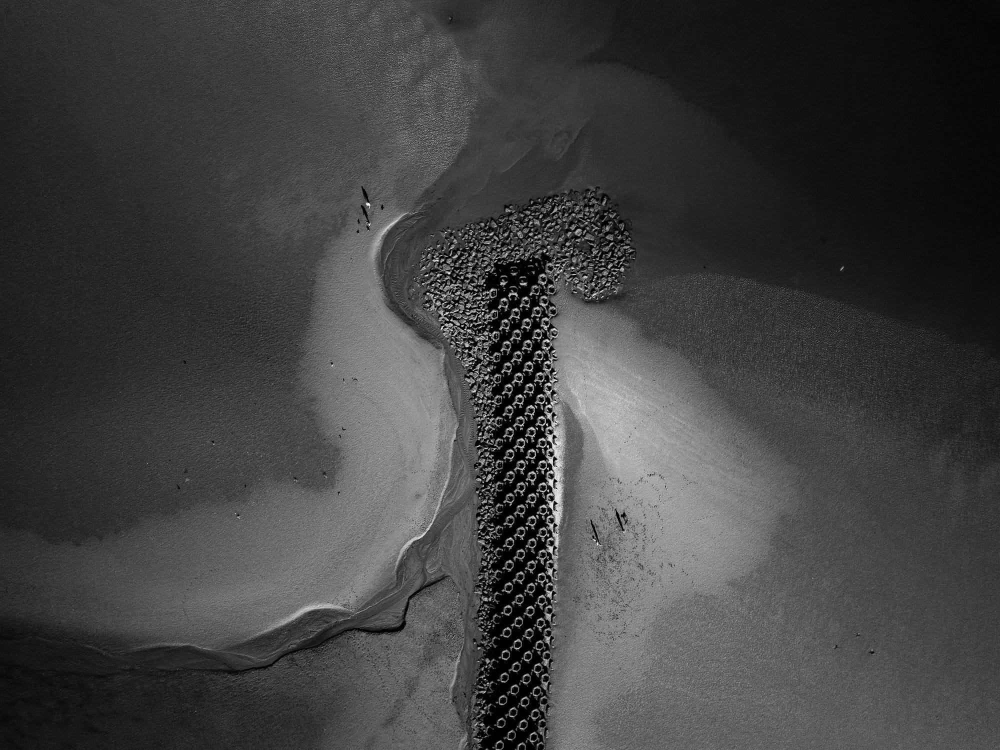 Aerial view of New Brighton beach at low tide, showing a breakwater and small figures on the sand.