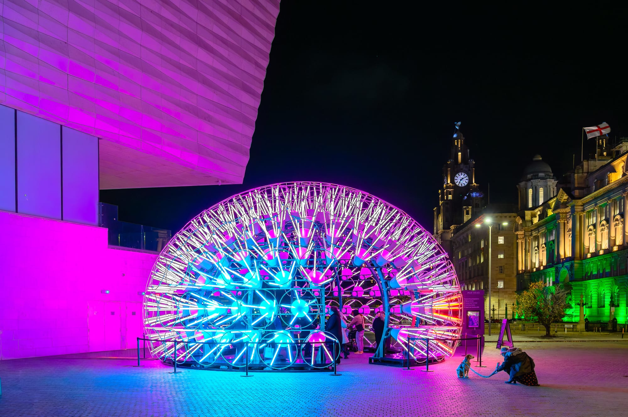 Night view of a light installation during the River of Light festival in Liverpool, with people and buildings in the background.