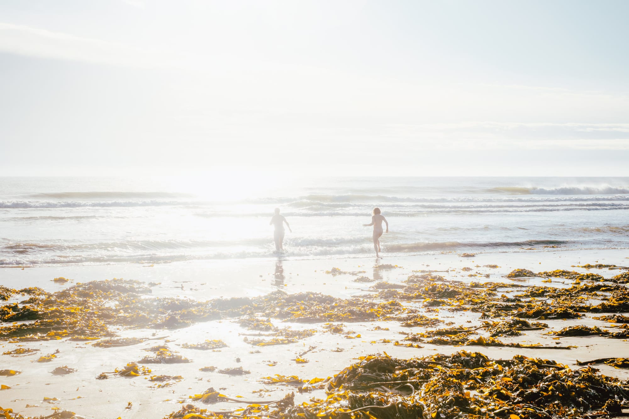At sunrise two naked people run into the sea.