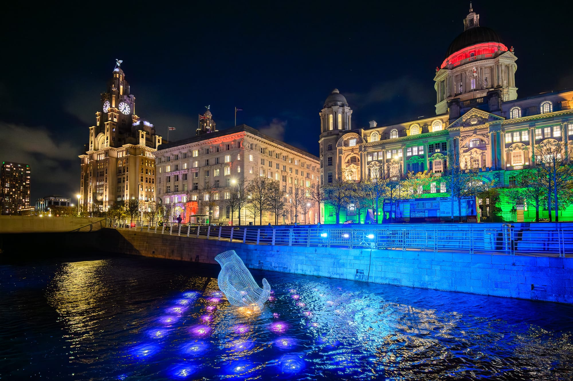 Night view of the Liver Building and the Royal Liver Building illuminated with colorful lights during the River of Light festival in Liverpool, England.
