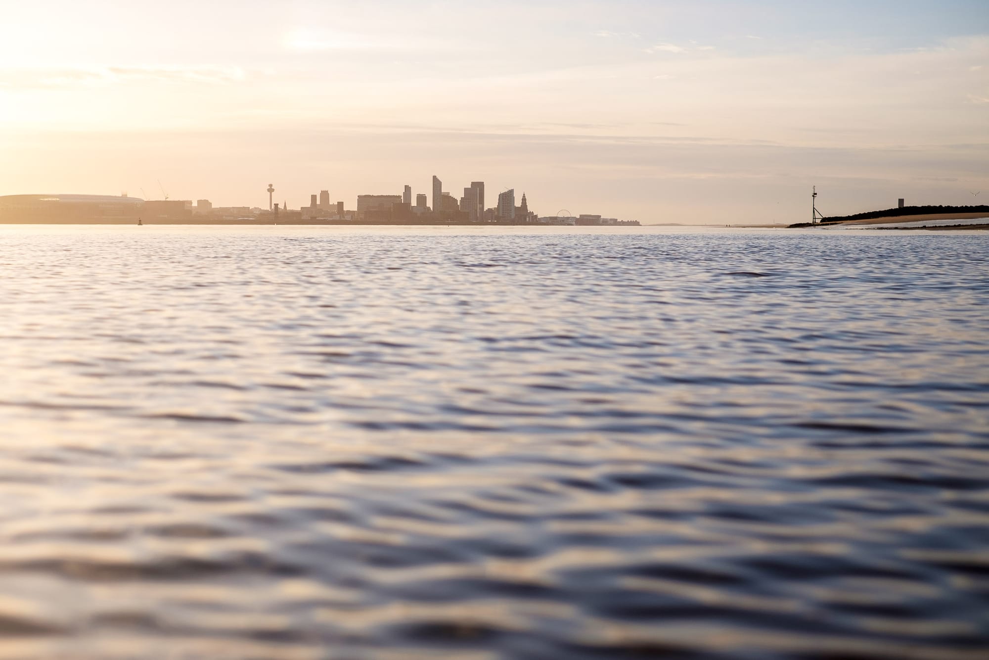 A hazy sunrise over a calm river Mersey with the city of Liverpool in the distance.