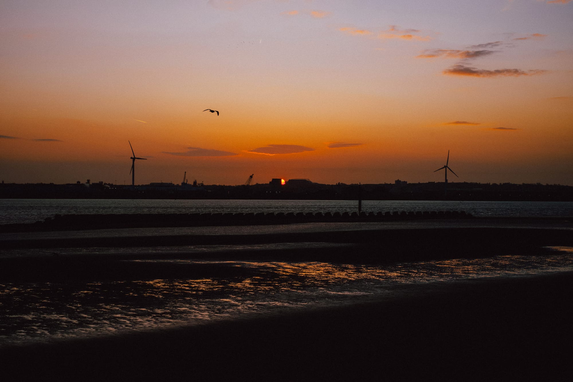 The sun rises behind some buildings across the River Mersey as the tide is out.