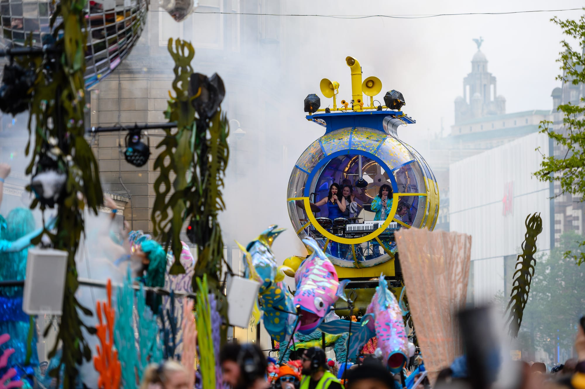 A yellow and blue submarine appears to float along a street in Liverpool filled with musicians.