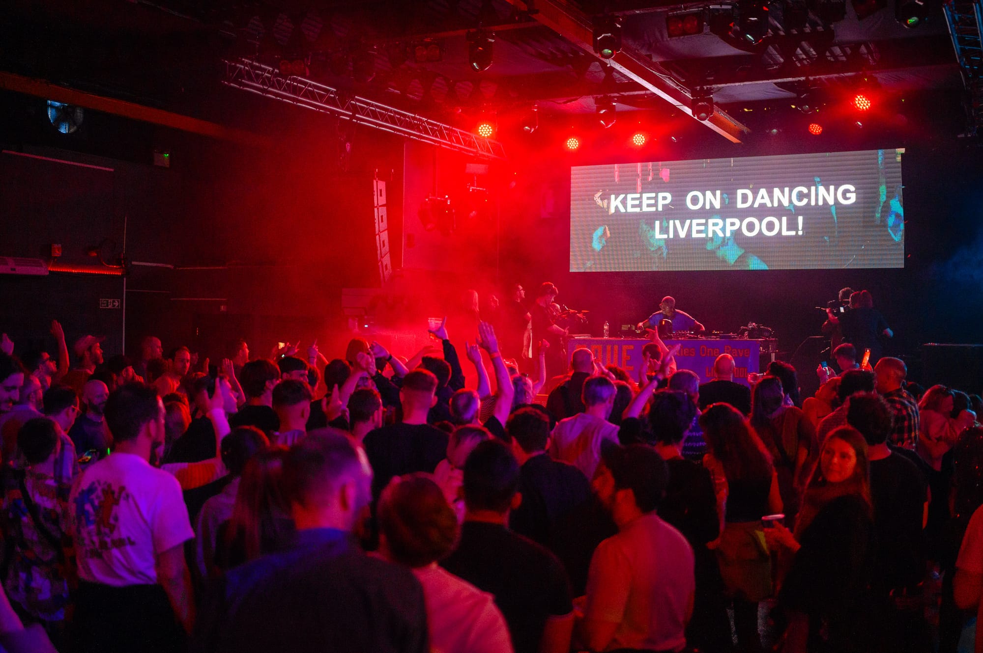 People dancing in a rave. On the screen it says 'Keep on dancing Liverpool!'