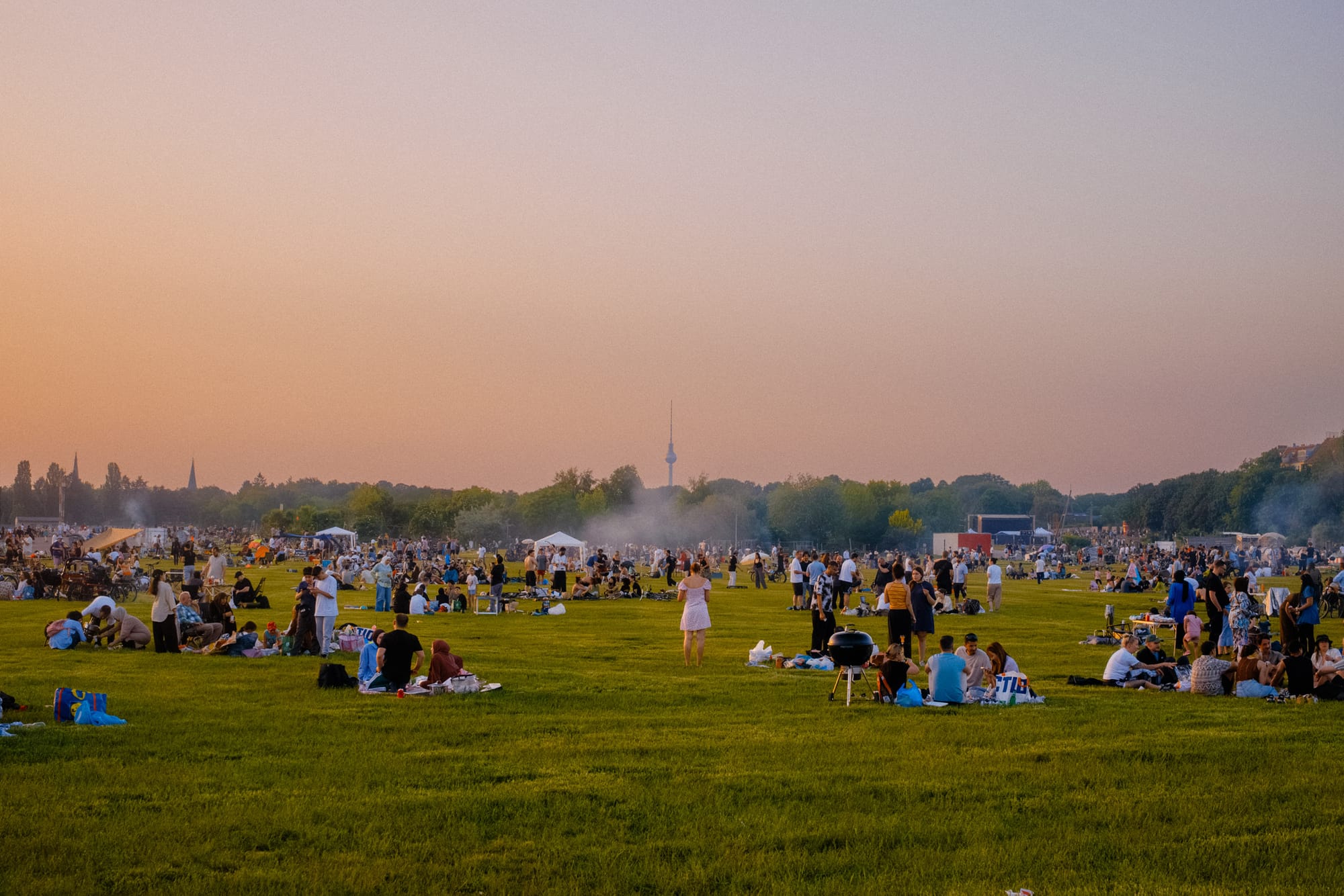 People gathering in a park with the Berlin TV Tower in the background.