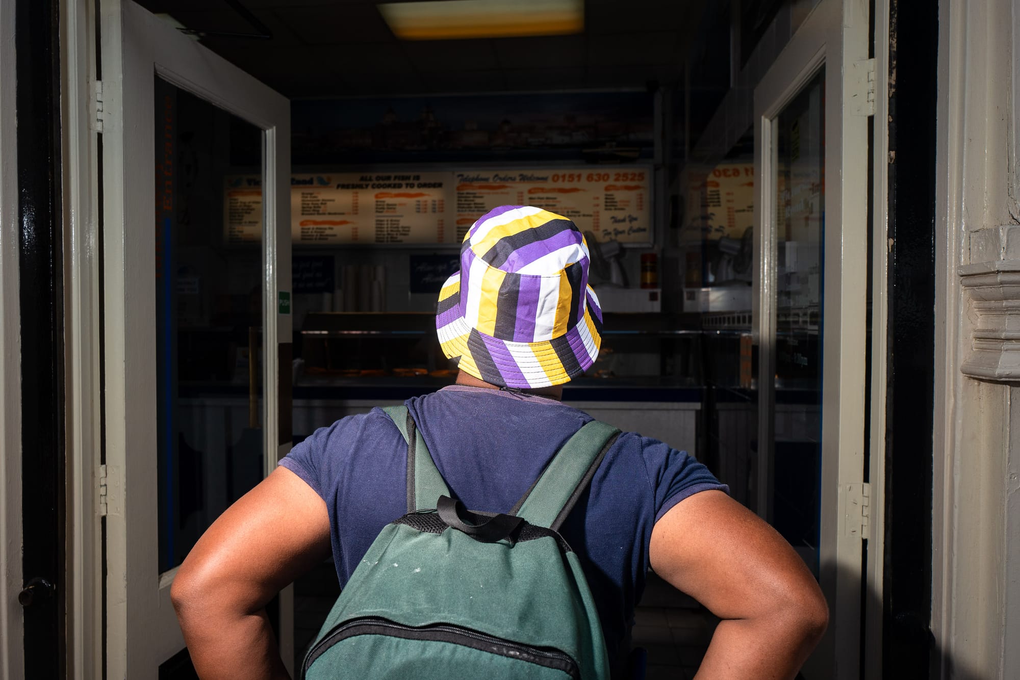 A person in a non-binary flag hat enters a chip shop.