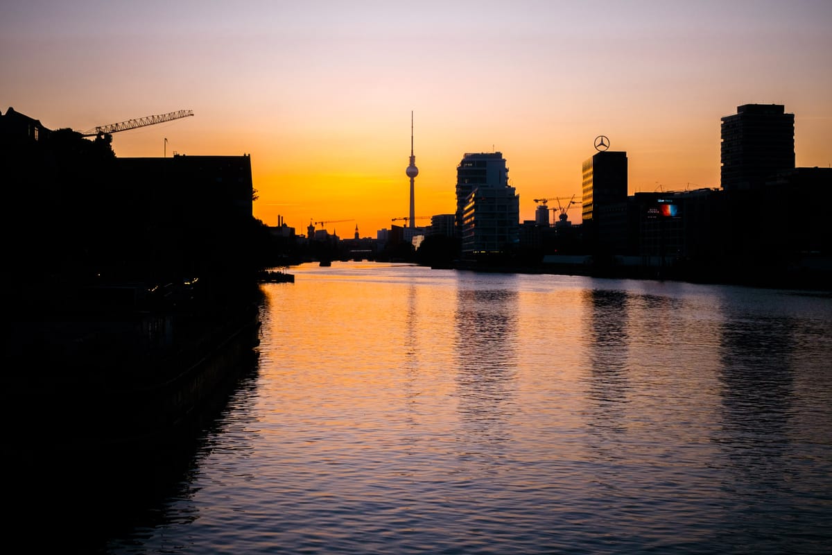 Silhouette of Berlin cityscape at sunset, with the Spree River in the foreground and the Berlin TV Tower prominently featured.