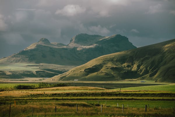 Lucious green fields extend across a mountain range on an overcast day.