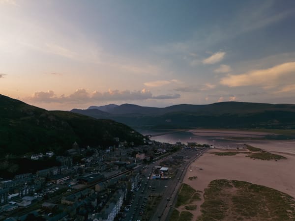 An aerial view of a coastal town at sunrise, showcasing a sandy beach bordered by rolling hills.