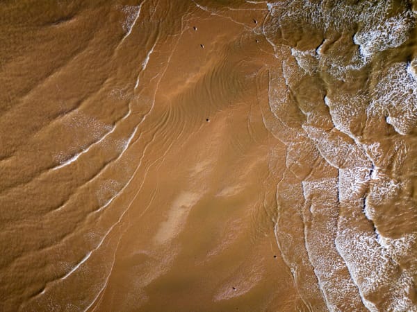 An aerial view of a sandy beach where gentle waves create a pattern on the shore.