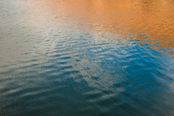 Abstract image of water surface with reflections in shades of blue, orange, and gray, with ripples and textures.