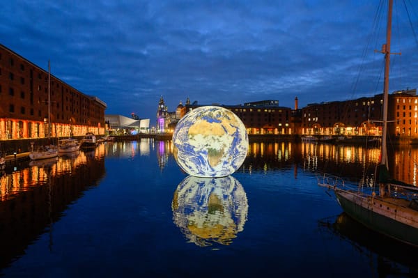 A 3D representation of the Earth floats inside Royal Albert Dock at dusk.