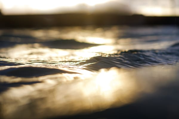 A close-up view of rippling water with a warm, golden light reflecting off its surface, creating a tranquil and dreamy atmosphere as the sun sets in the background.