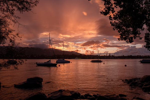 Sunset over Lake Geneva. Clouds roll over the mountains in the distance and yachts bob about on the lake.
