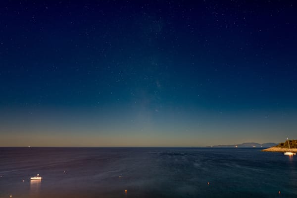 A starry night sky over a body of water with some islands in the distance.