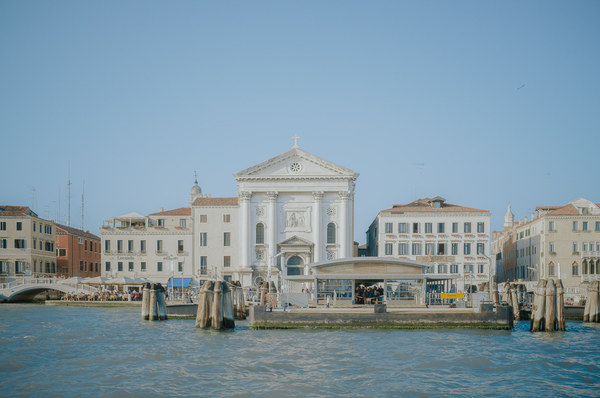 Venice. Tall white buildings stand against a blue sky. The middle one has columns and a cross on top.