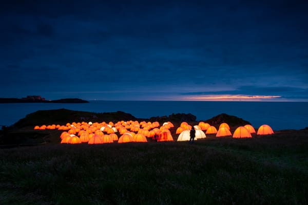 Glowing orange tents sitting on top of a cliff in North Wales at dusk.