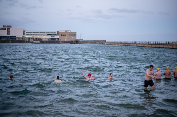 People swimming in a lake. In the middle a non-binary person in a red hat smiles and does thumbs up to the camera.