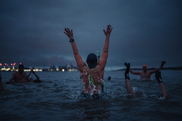 A woman jumps up in the water at dawn. The city of Liverpool is on the horizon.