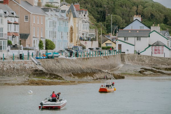 A couple of small boats sailing down a river outside some pastel coloured houses.