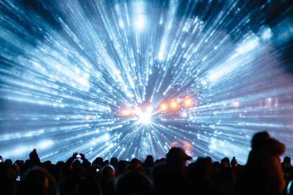 Star warp effect projected onto water vapour at night with crowd in front.