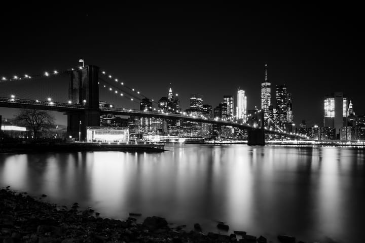 The New York skyline at dusk. The Brooklyn Bridge is covered in lights stretching across the river to Manhattan.