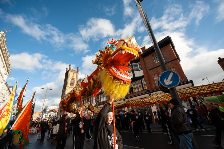 Performers hold a Chinese Dragon puppet aloft on a sunny day.