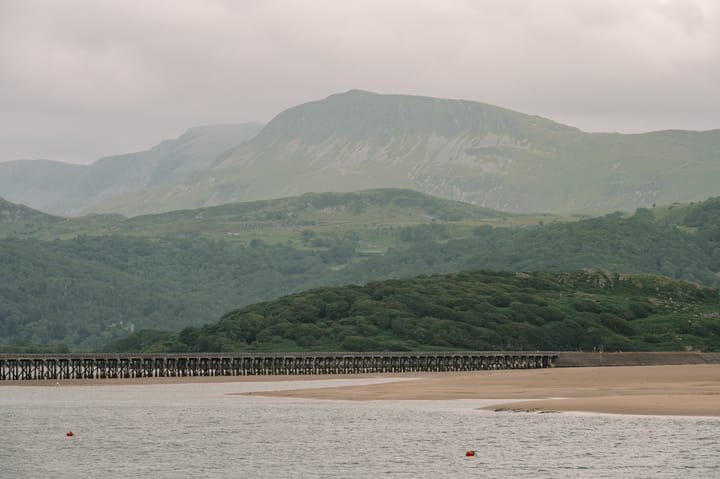 Mountains fade into the distance and a railway bridge runs over an estuary.