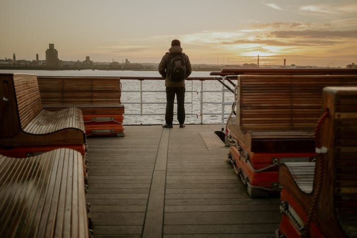A person stands by the railings on a ferry and watches sunset.