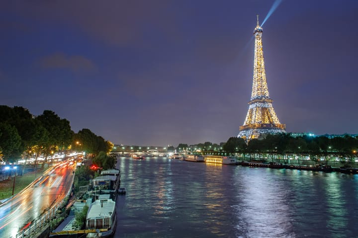 The Eiffel Tower stands tall above the River Seine in Paris. The search light is panning across the skyline of Paris.