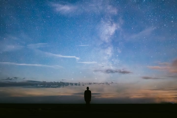 A silhouetted person stands looking up at the Milky Way Galaxy.