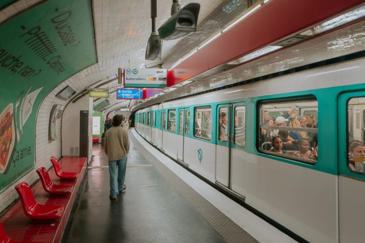 In a Parisian subway station a man wearing headphones walks past a subway train.