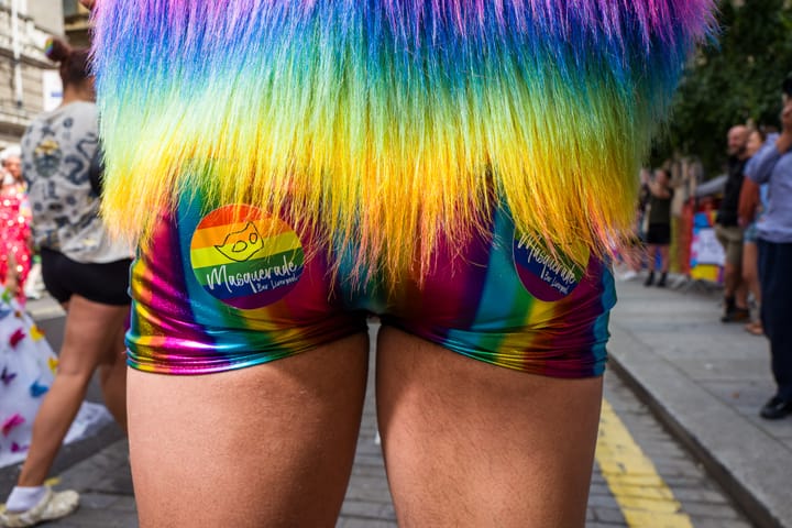 A male bottom. The person is wearing shiny rainbow hot pants. 