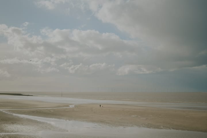 A lone figure walks along an empty beach as the tide is out.