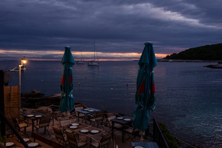 Dusk with a hint of red sky on the horizon. There's a resturant with tables set out by the open sea. 