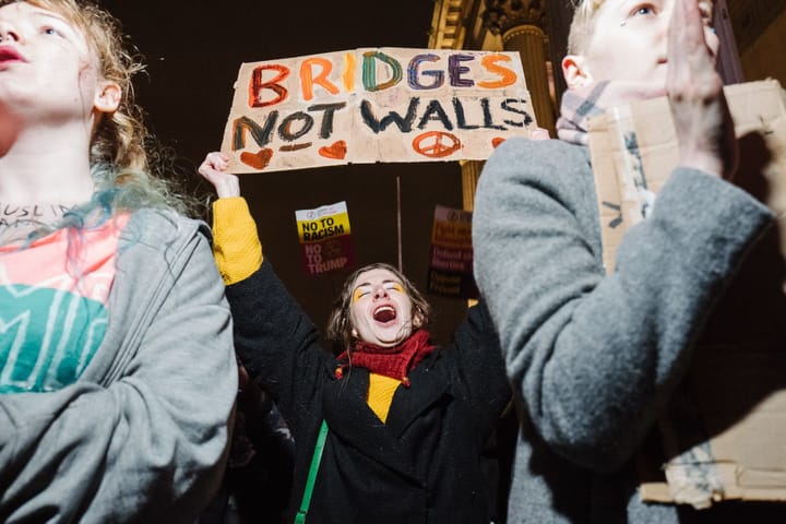 A woman holds up a sign saying "Bridges not walls". Bridges is in rainbow colours.