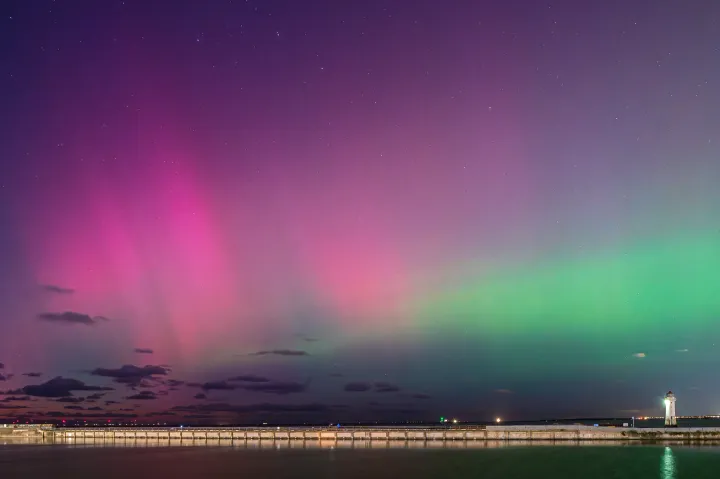 A green and pink aurora over a marine lake near a lighthouse.