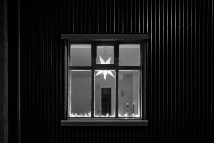 A black and white scene from outside a house. Through a singular window 