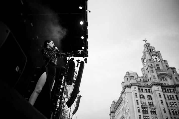 A black and white photo of a performer on stage with a building in the background.