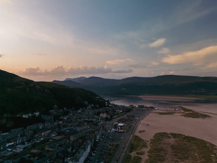 An aerial view of a coastal town at sunrise, showcasing a sandy beach bordered by rolling hills.