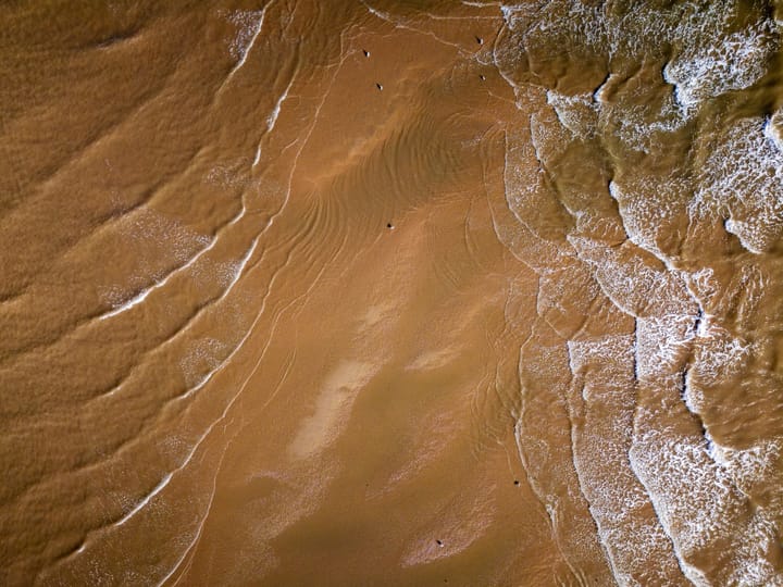 An aerial view of a sandy beach where gentle waves create a pattern on the shore.