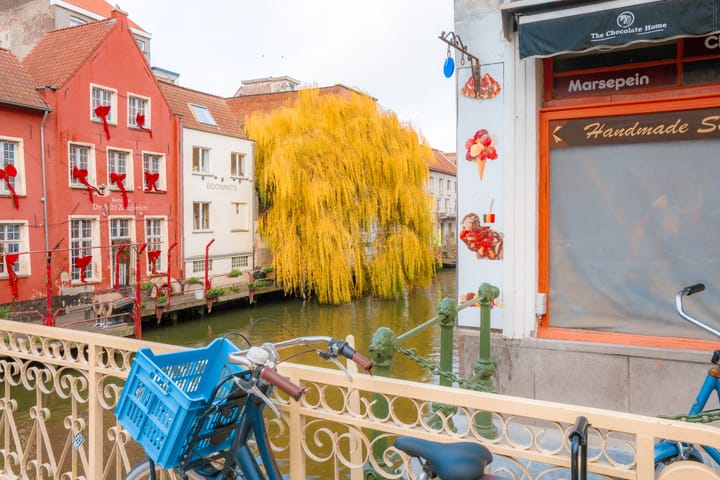 A bicycle parked on a bridge in Ghent, Belgium, with colorful buildings and a canal in the background.