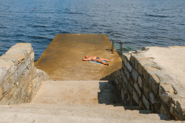 A man sunbathing on a concrete pier near the sea.