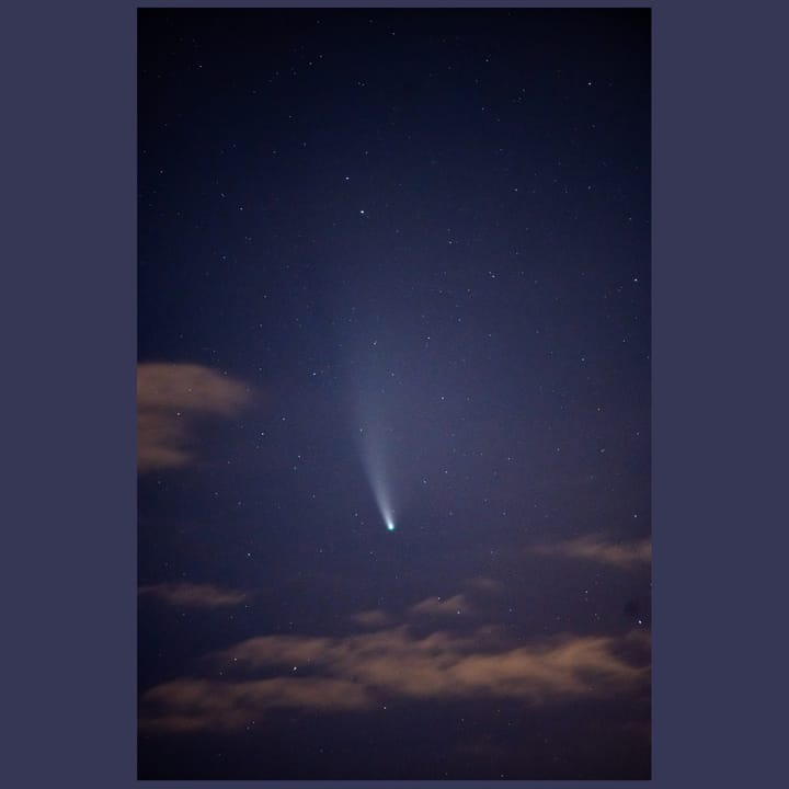 A comet with a whispy white tail flies through the nights sky.
