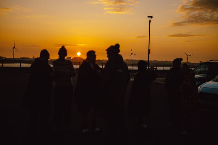 Swimmers meeting at sunrise in a car park by the river.