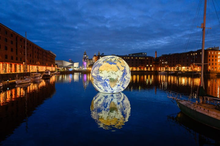 A 3D representation of the Earth floats inside Royal Albert Dock at dusk.