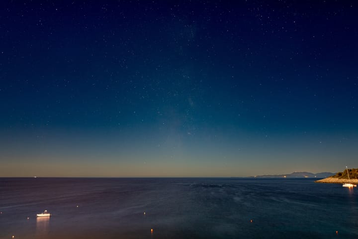 A starry night sky over a body of water with some islands in the distance.
