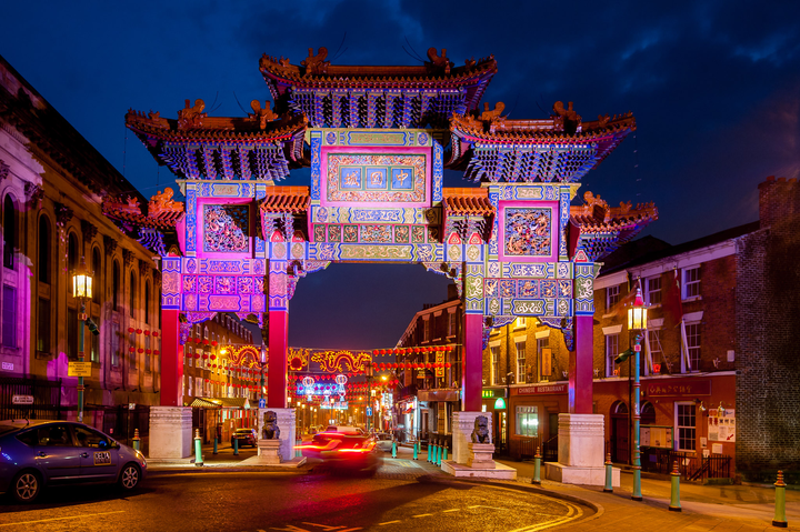 A large Chinese arch lit up at night in purple with a car going through it.