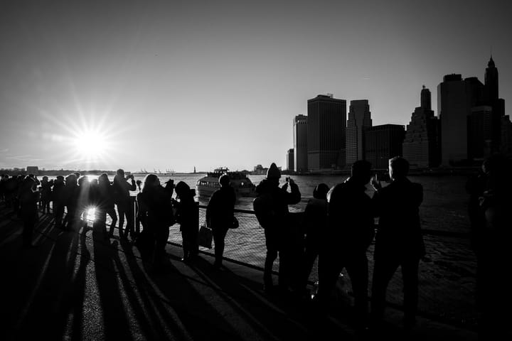 Black and white photo. People taking photos from Brooklyn promenade of the Manhattan skyline.